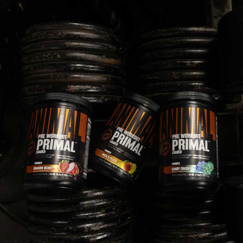 Three bottles of Primal Pre Workout on a dark background with weights.